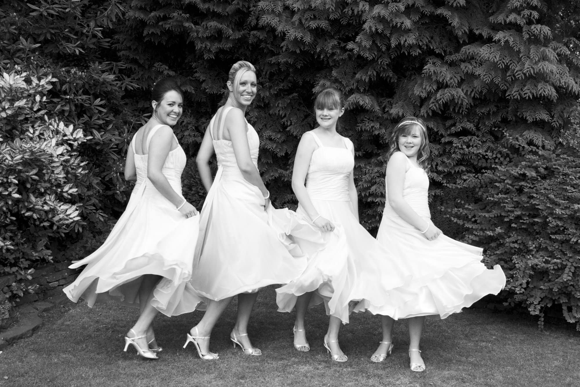 Bridesmaids swinging their dresses in garden before ceremony in wedding photography by Bromley photographer
