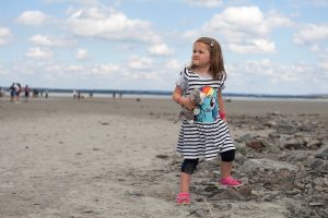 Photo of girl under clouds cuddling toy on French beach
