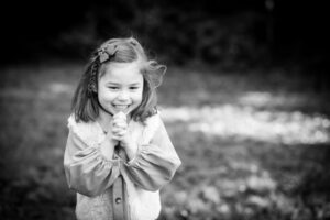 Happy girl holding hands and smiling outside in park on family photoshoot in Bromley