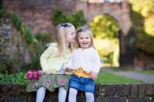 sisters with flowers sat on wall and photographed in Bromley