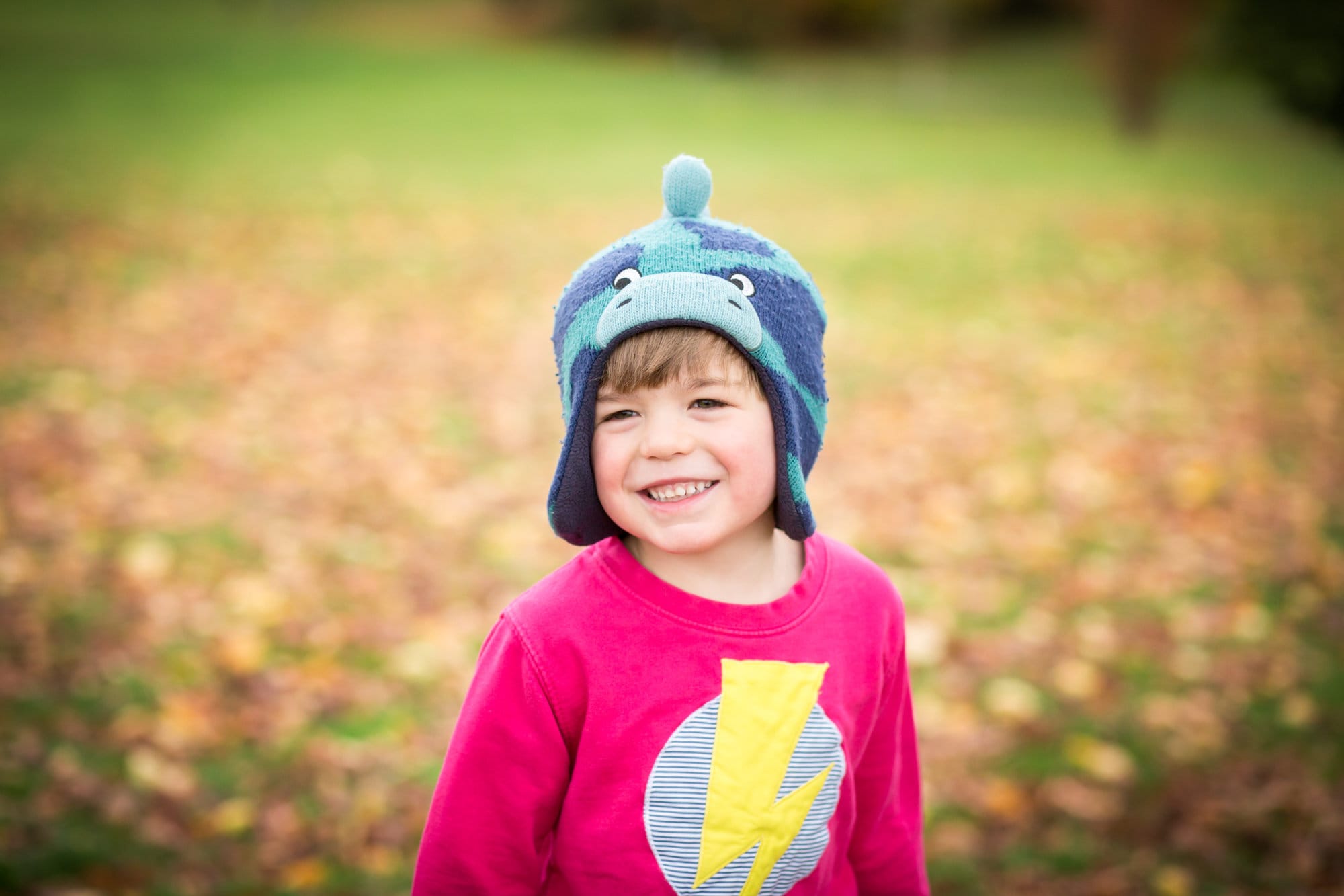 Smiling boy stood in autumn leaves in Beckenham Place Park by London family photographer