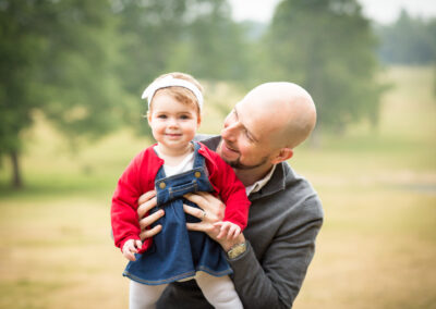 Bromley photoshoot of little girl in red cardigan being held by Dad outside in park