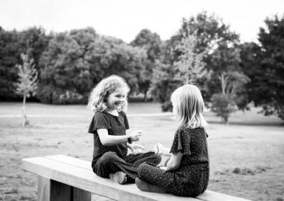 Sisters playing game on bench in Beckenham Place Park family photoshoot in Bromley