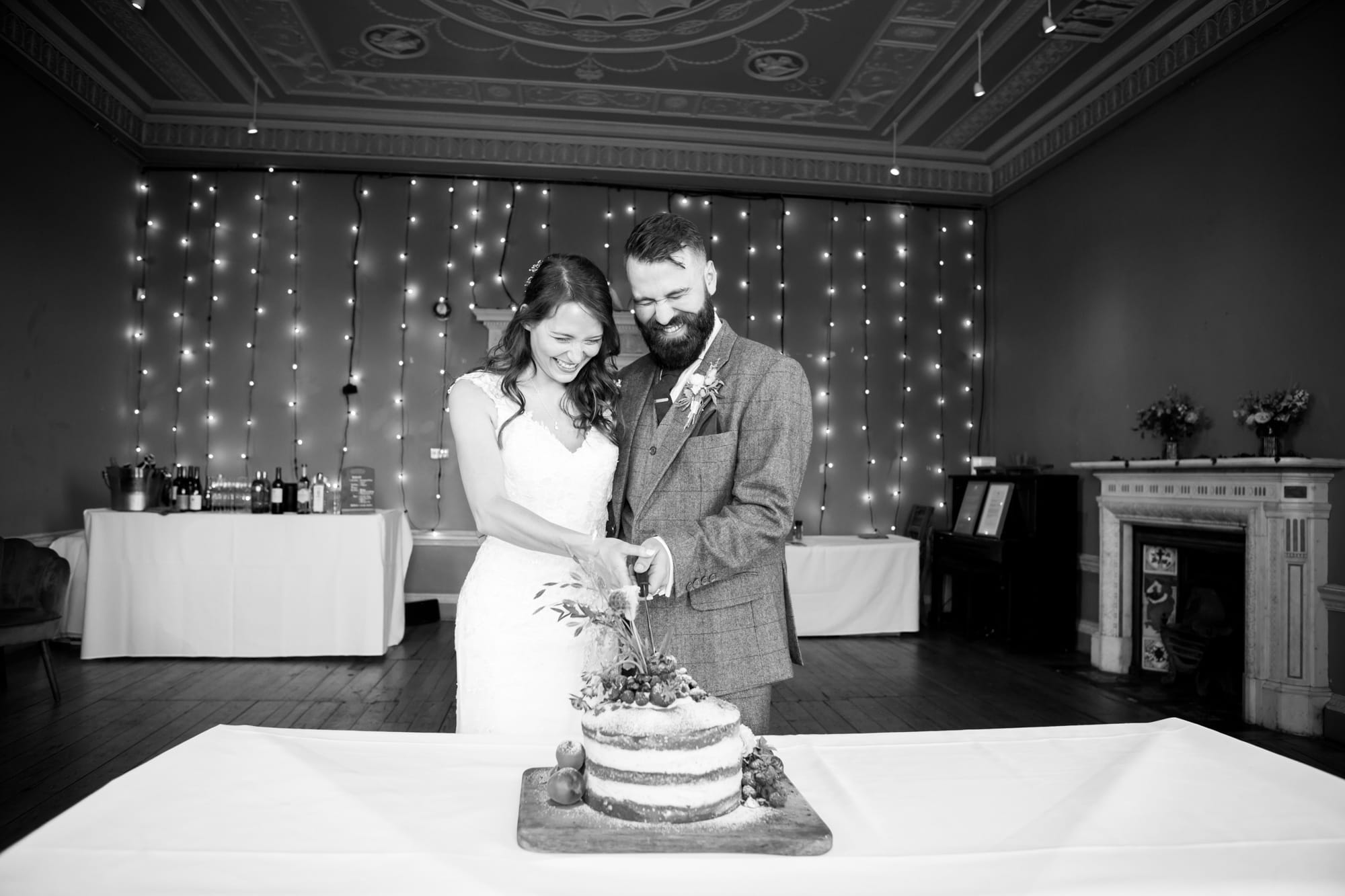 Black and white wedding photo of couple laughing and cutting their cake at Beckenham Place Mansion wedding venue