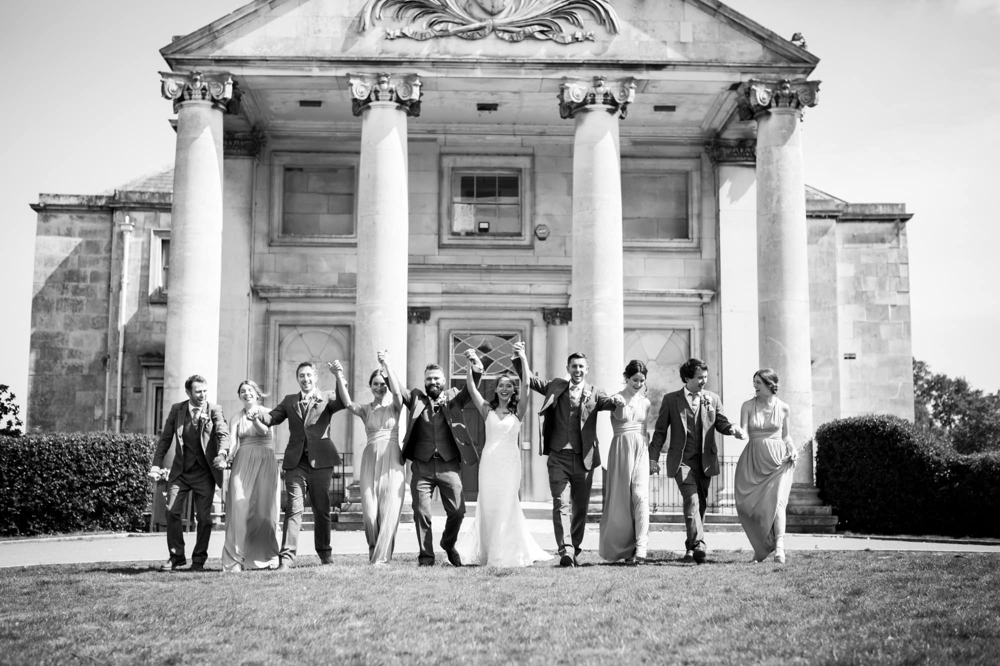 fun bridal party image of everyone holding hands and walking taken outside Beckenham Place Mansion by Bromley Wedding Photographer in black and white
