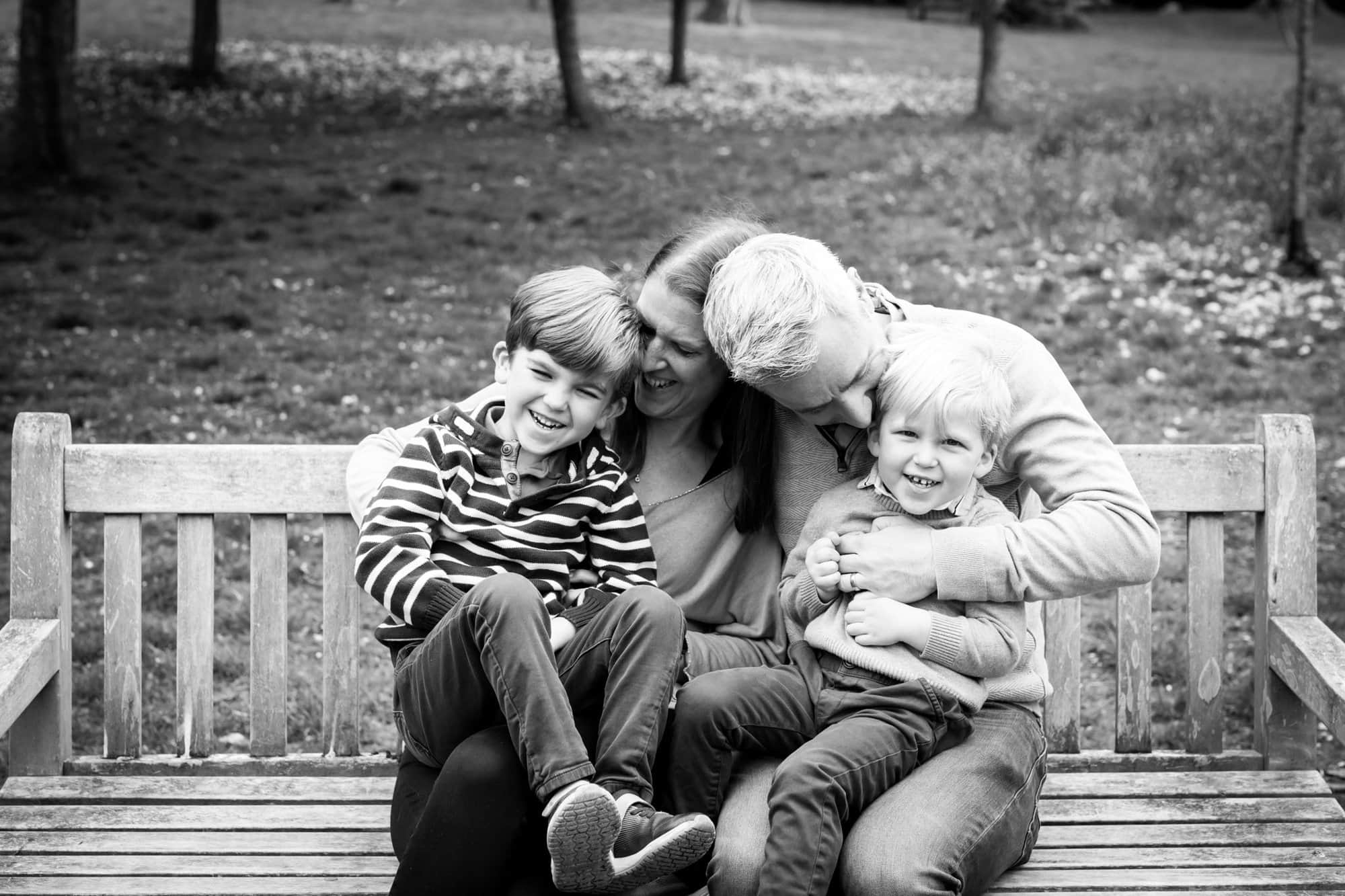 Photoshoot in Bromley of family tickling and children laughing on park bench in black and white image