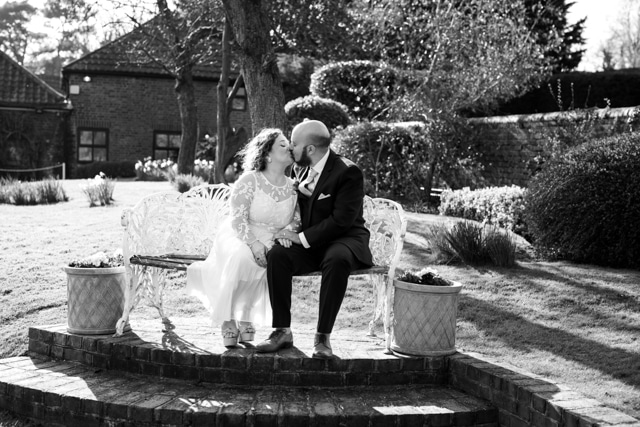 black and white wedding photo of couple sat on bench at Oaks Farm Weddings taken buy Bromley wedding photographer