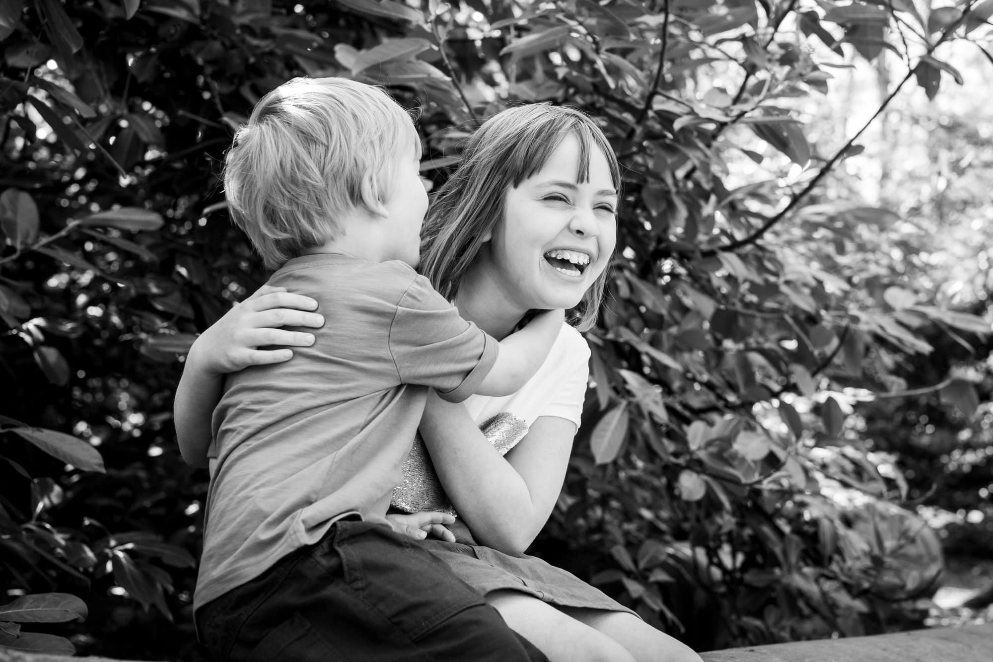 Brother whispering into sisters ear and making her laugh in black and white photo in photoshoot in Bromley by Tessa Clements