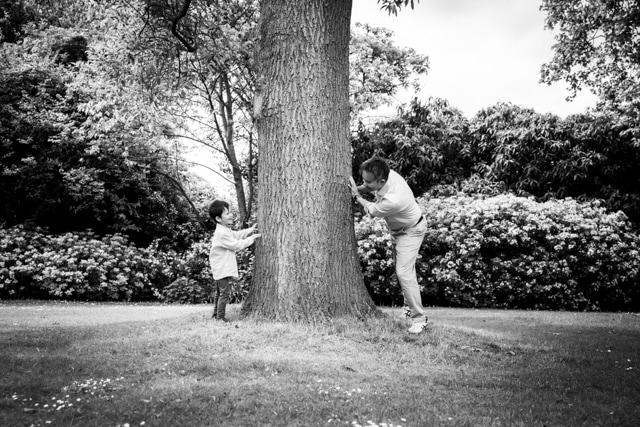 Father and son playing peek-a-boo round a tree in black and white photo taken by Bromley photographer