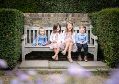 Siblings sat on bench and looking away from camera with flowers in foreground taken by Bromley Photographer