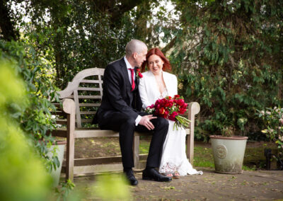 Bride and groom sat on bench smiling after wedding. Wedding photography in Bromley