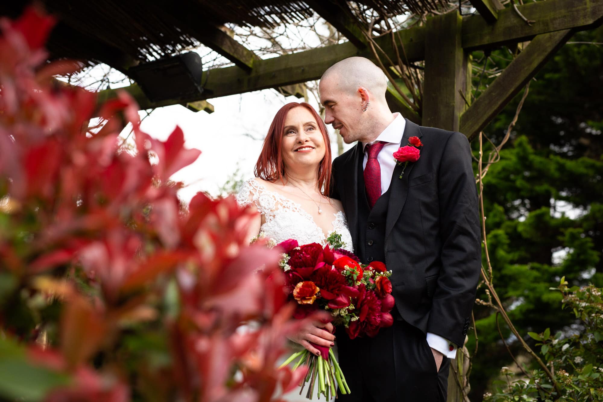 Bromley wedding photography image of couple standing by red spring flowers at Oaks Farm Weddings venue