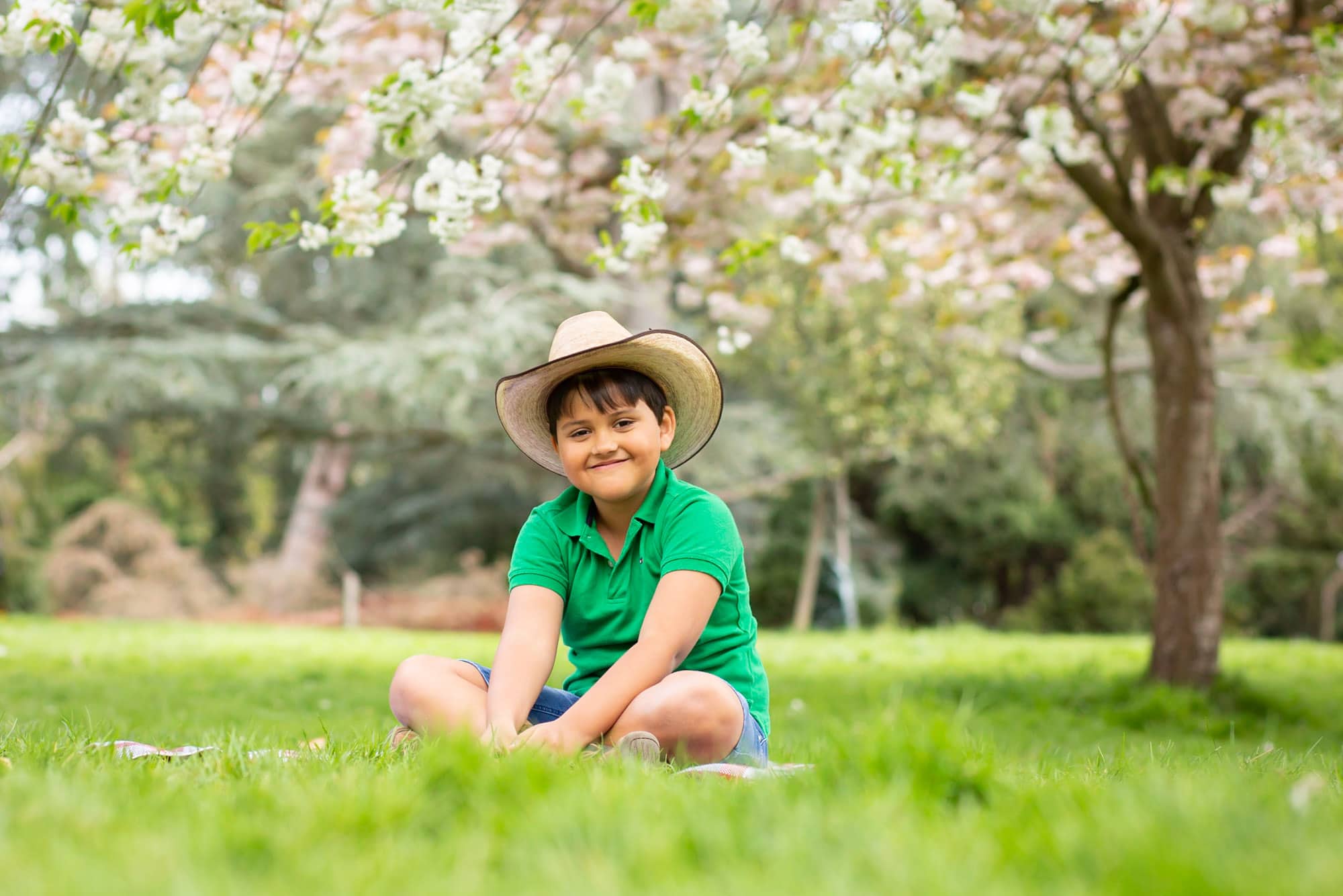 boy sat on grass among spring blossom with cowboy hat on taken by Beckenham family photographer 