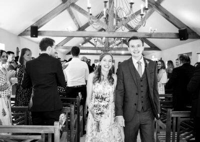 Bride and groom walking out of ceremony smiling in black and white photograph taken by Bromley photographer