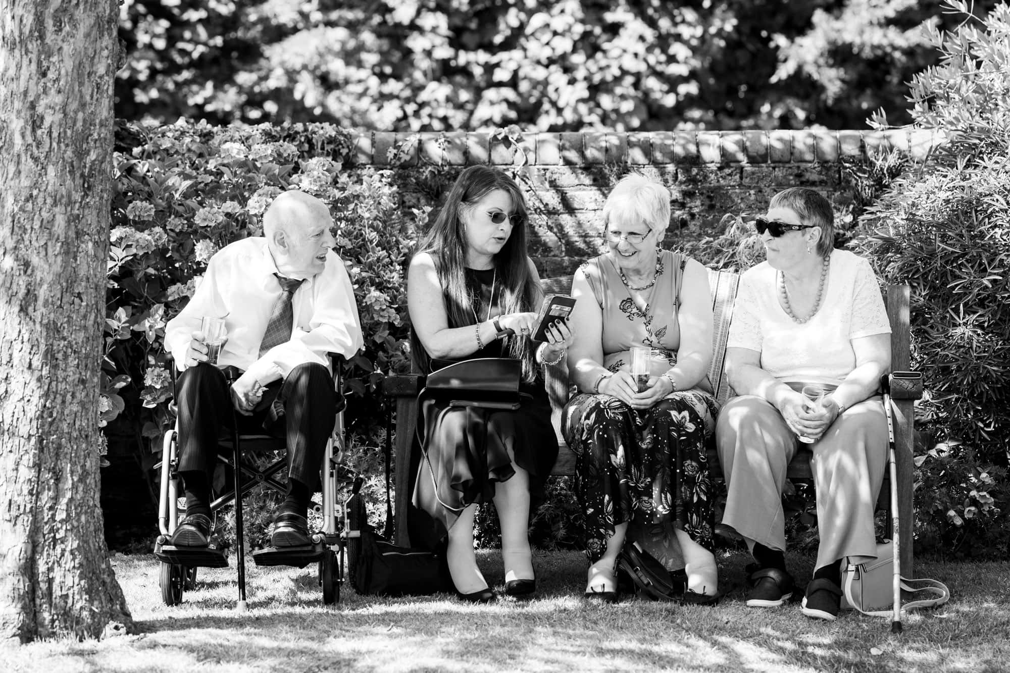 Guests chatting on bench in black and white wedding photo taken at Oaks Farm Weddings