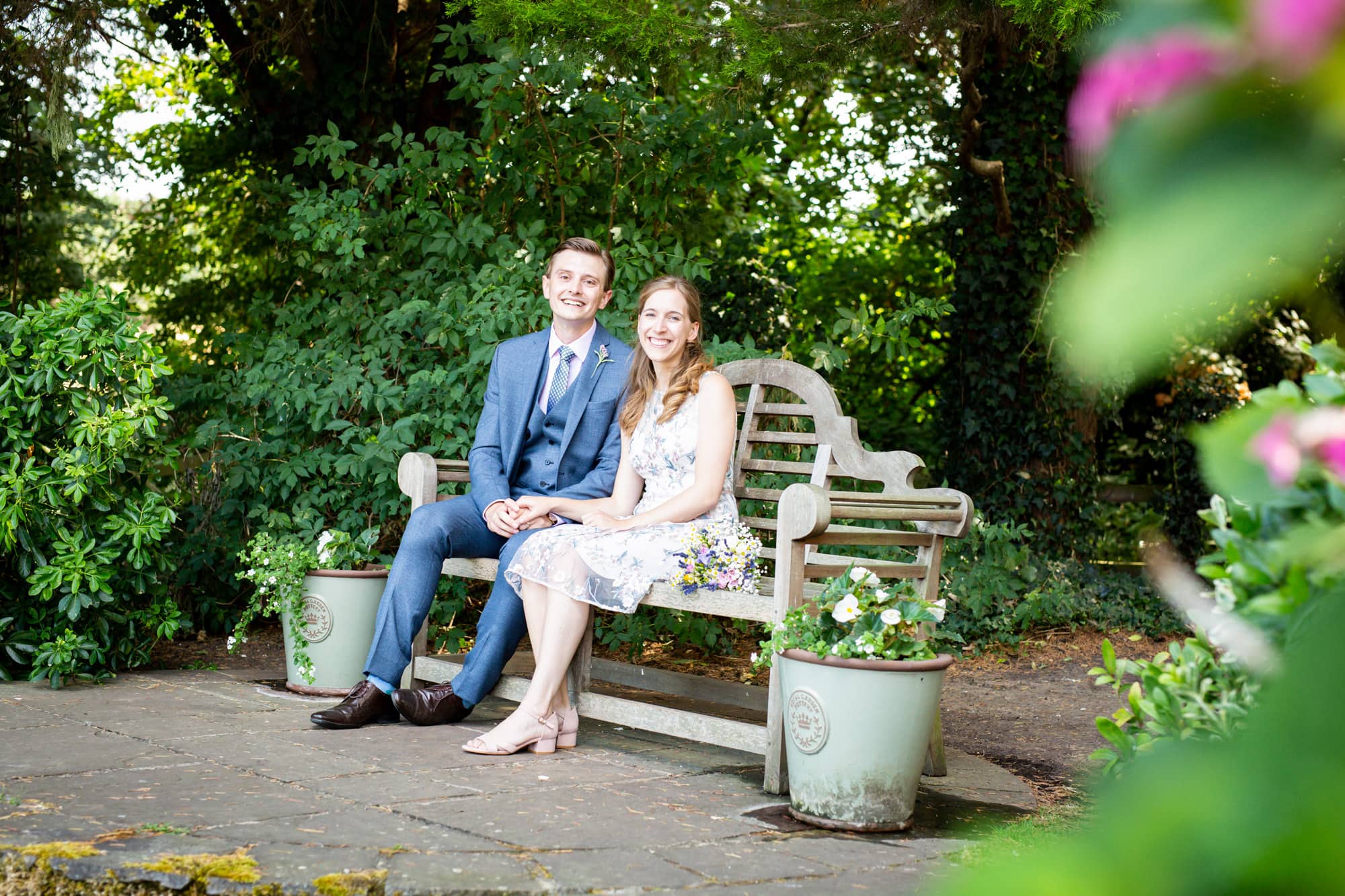 Smiling bride and groom sat on bench at Oaks Farm Weddings in Bromley wedding photoshoot