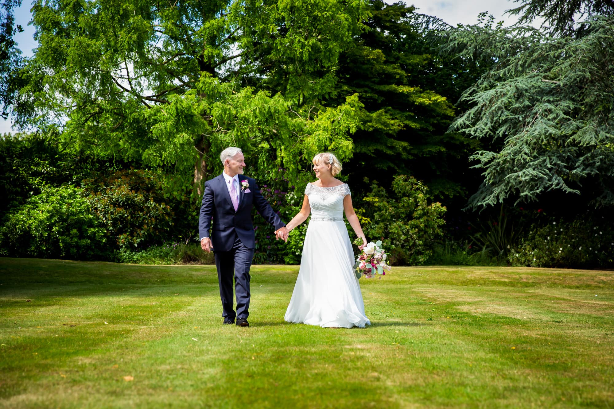 Couple holding hands and walking on grass on wedding day at Oaks Farm Weddings venue taken by Beckenham Wedding Photographer