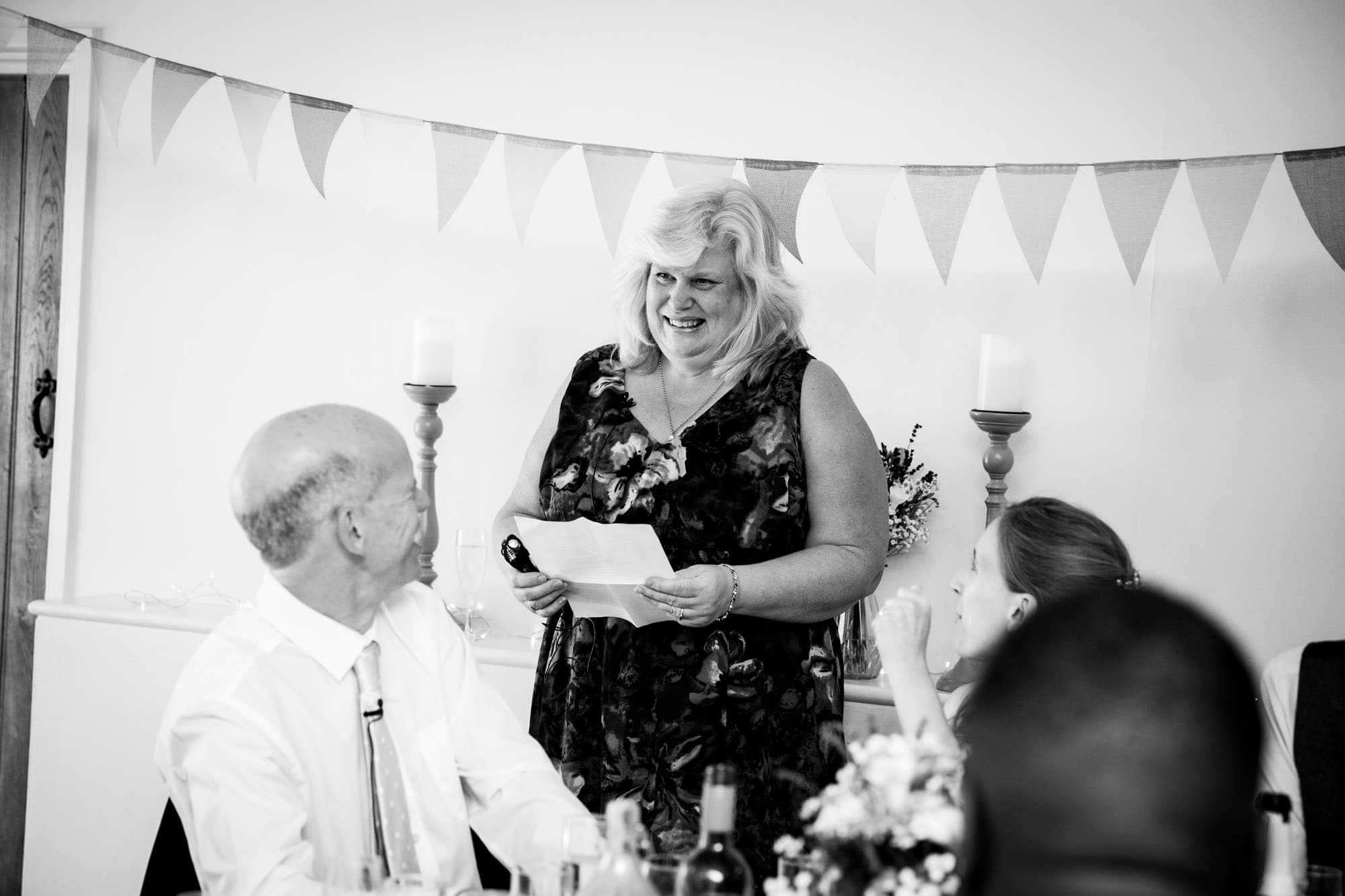 Guest reading out their speech and smiling in black and white wedding photo by Bromley wedding photographer at Oaks Farm Weddings