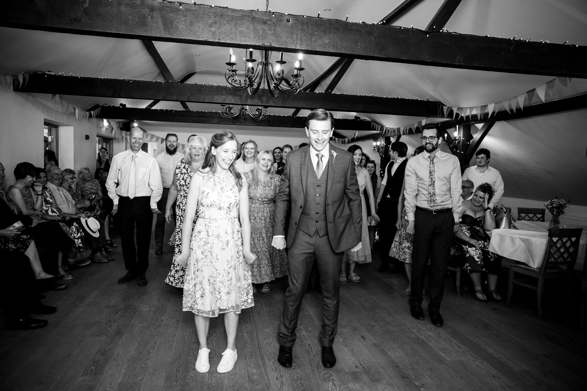 Black and white photo of bride and groom getting ready for group line dance at wedding reception at Oaks Farm Weddings taken by Bromley wedding photographer